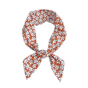Orange linen-cotton scarf with white floral print tied in a loop on a white background