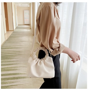 Detail of beige pleated handbag with ruched handle and gold metal hooks on a shoulder strap