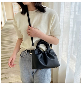 Woman wearing a black pleated cloud bag with gold hardware and slim shoulder strap