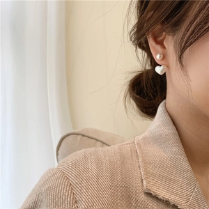 Detailed close-up of a model wearing minimalist heart-shaped pearl earrings in a beige suit