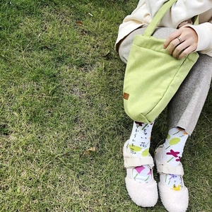 Detail of light green tote bag and white Tabi socks with floral patterns on grass