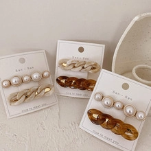Detail of cream acrylic chain hair clips and faux pearl barrettes on stone background