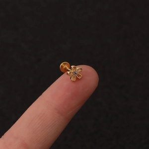 Detailed close-up of tiny golden flower labret stud with pink zircon on a fingertip