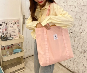 Minimalist pink canvas tote bag showing model fit and large capacity on white brick wall