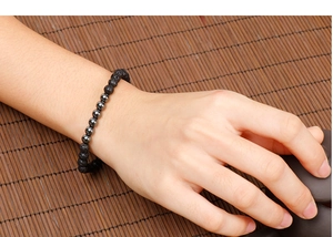 Close-up of black lava stone and hematite beaded bracelet worn on a wrist over a zen mat
