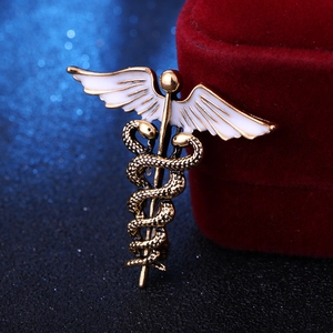 Close-up of golden caduceus brooch with white enamel wings on red velvet box