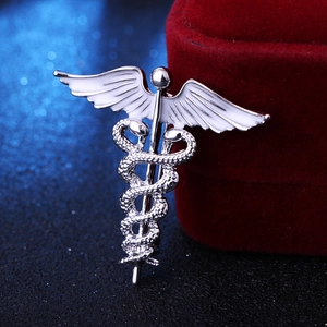 Detail view of silver Caduceus snake brooch with white enamel wings on velvet