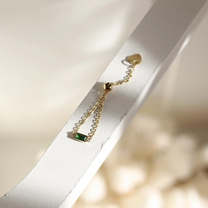 Macro detail of adjustable gold chain ring featuring a green emerald-cut zircon and heart charm