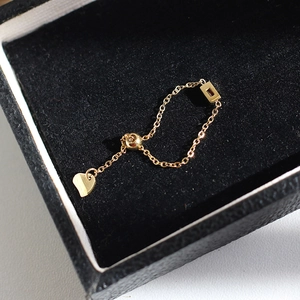 Close-up of adjustable gold chain ring with red gemstone and heart charm detail