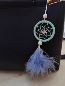 Detail of dream catcher bag charm with light teal ring and blue feathers on a bag