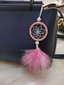 Pink dreamcatcher bag charm with soft feathers and beads on a blue handbag handle