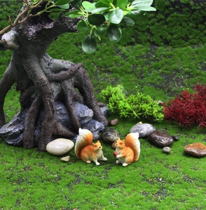 Dettaglio di due statuine di scoiattolo in resina con noci in un micro paesaggio di muschio