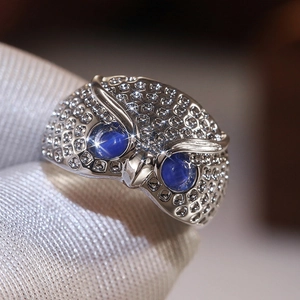 Macro shot of owl ring with blue sapphire eyes and pavé crystals on silver metal