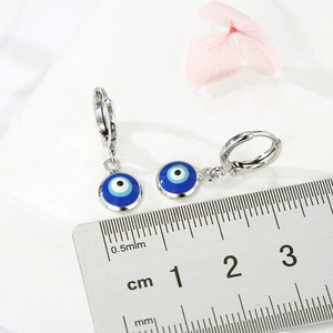 Silberne Creolen mit blauem Evil-Eye-Anhänger neben einem Lineal zur Größenmessung