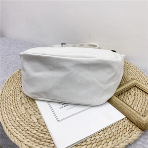 White canvas shoulder bag with thick fabric texture shown on a woven mat