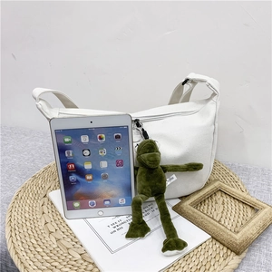 Detail of white canvas crossbody bag with green frog pendant and iPad for size scale