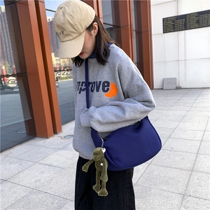 Detail of navy canvas crossbody bag with green plush frog charm on model in urban setting