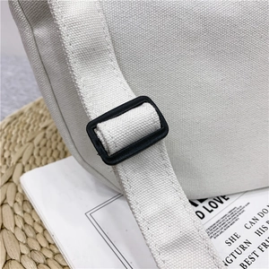 Detailed close-up of adjustable strap buckle on a cream canvas crossbody bag