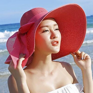 Detail of red wide-brim straw hat featuring a soft bow accent for beach sun protection