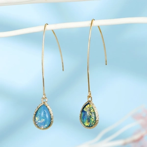 Macro detail of teardrop resin opal earrings with gold trim on light blue silk