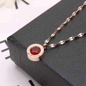 Détail du collier en or rose avec une pierre rouge et pendentif gravé de chiffres romains