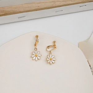 Detail shot of daisy clip-on earrings with white petals and golden accents on a white stand