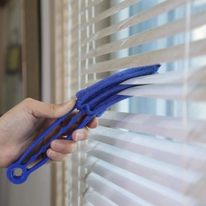 Close-up of hand using blue microfiber brush tool to clean white window blinds