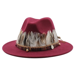 Dettaglio di cappello in lana con piume, nastro etnico e ciondoli a moneta metallici