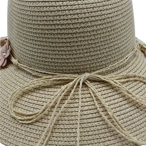 Close-up of the beige woven straw hat texture with a pink flower and bow accent