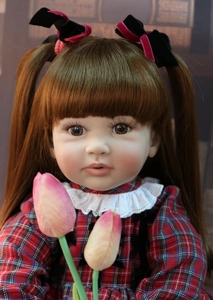 Close-up of 60cm reborn doll with auburn pigtails, red plaid dress and pink tulips