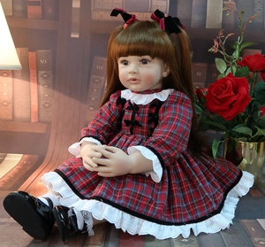 Detailed view of 60cm reborn toddler doll in red plaid dress seated by a bookshelf