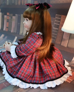 Detailed view of reborn toddler doll in red plaid dress seated by vintage books