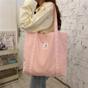 Side view of large pink canvas tote bag worn by model against a white brick wall