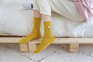 Detail of yellow ribbed mid-tube socks with daisy embroidery and ruffled lace cuffs