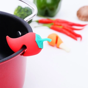 Detail of red chili-shaped silicone lid lifter preventing overflow on a pot rim