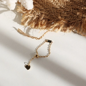 Detail of adjustable gold chain ring with black gemstone and heart charm on white background
