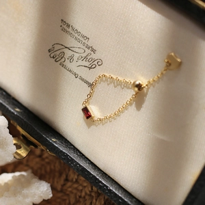 Detail of adjustable gold chain ring with emerald cut red zircon in a vintage jewelry box