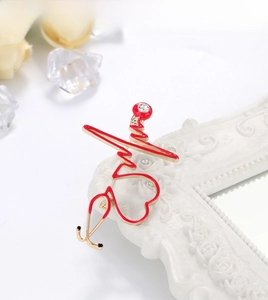 Detail of stethoscope brooch with red enamel heart and crystal on white frame