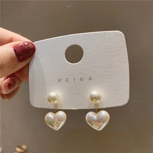 Detail of heart-shaped pearl earrings with gold base on a REINA display card