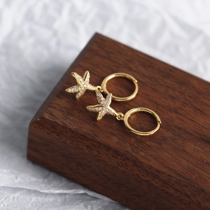 Detailed view of gold starfish earrings with clear crystals on a dark wood base