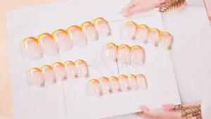 Detailansicht der orangefarbenen French Press-on Nails mit weißen Perlenverzierungen