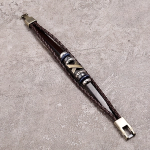 Detail of multi-layer brown braided leather bracelet with bronze X-shaped alloy charm