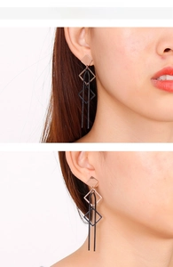 Détail de boucles d'oreilles losanges avec de longs glands noirs en finition or rose