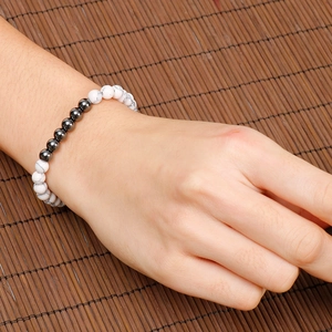 White turquoise and dark grey beaded stretch bracelet on a female wrist over a bamboo mat