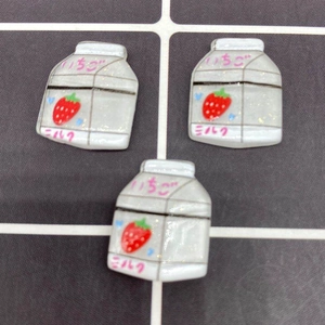 Three mini resin strawberry milk bottle charms with Japanese text on a grid background