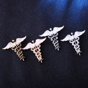 Set of four caduceus pins in gold and silver finishes with white enamel angel wings