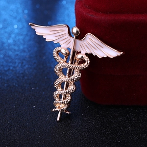Close-up of golden caduceus brooch with white enamel wings on a red velvet jewelry box