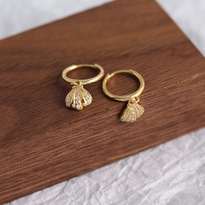 Macro shot of gold shell hoop earrings with inlaid white zircons on a wooden base
