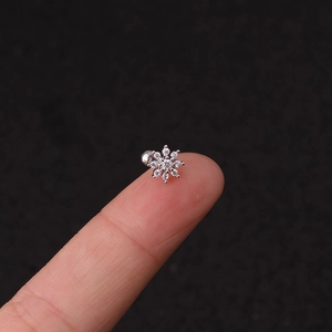 Macro shot of silver flower piercing stud with clear zircons held on a fingertip