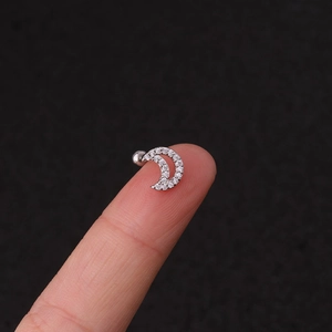 Macro shot of silver crescent moon cartilage earring with zircon held on fingertip